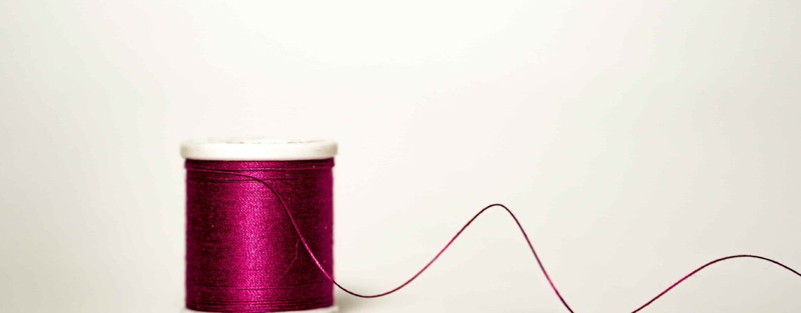 A spool of pink thread with a tail of thread running off to the right of the photo